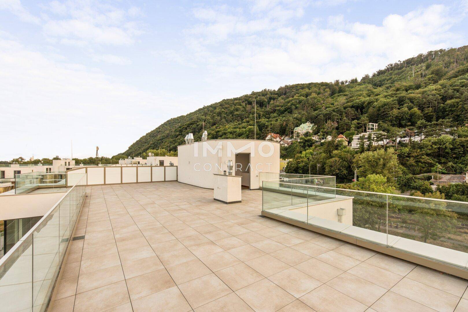 Geräumige Dachterrasse mit moderner Architektur und weitem Blick auf die bewaldeten Hügel.