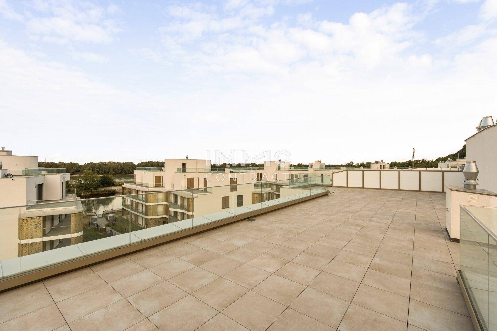 Ausgedehnte Dachterrasse mit Fliesenboden und Glasbrüstung, bietet weite Ausblicke.