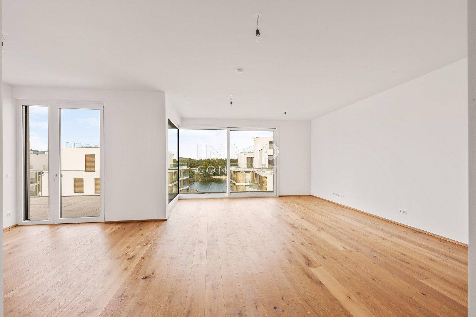 Helles Wohnzimmer mit Holzboden und großen Schiebetüren, die auf eine Terrasse führen und Seeblick bieten.