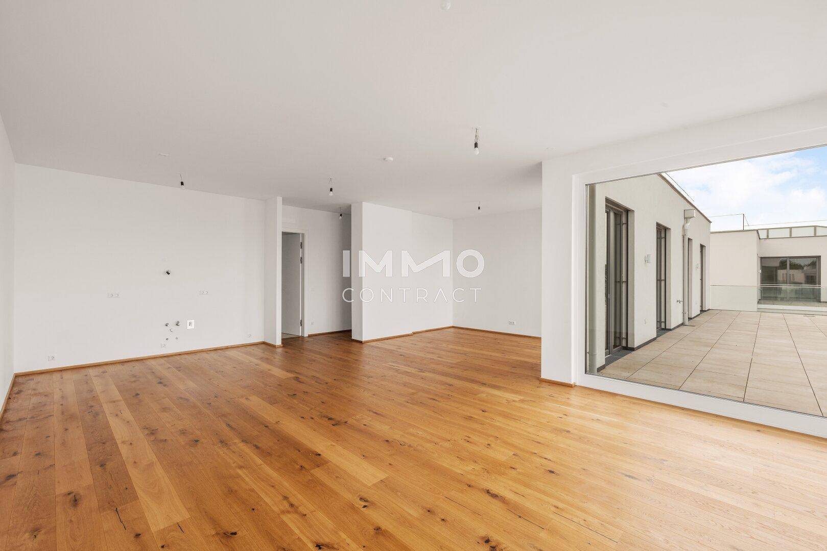 Geräumiges, unmöbliertes Wohnzimmer mit Holzboden und Zugang zu einer großen Dachterrasse.