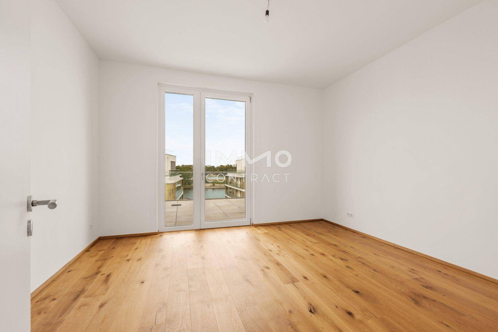 Leeres Schlafzimmer mit Holzboden und Fenstertür, die Zugang zu einem Außenbereich bietet.