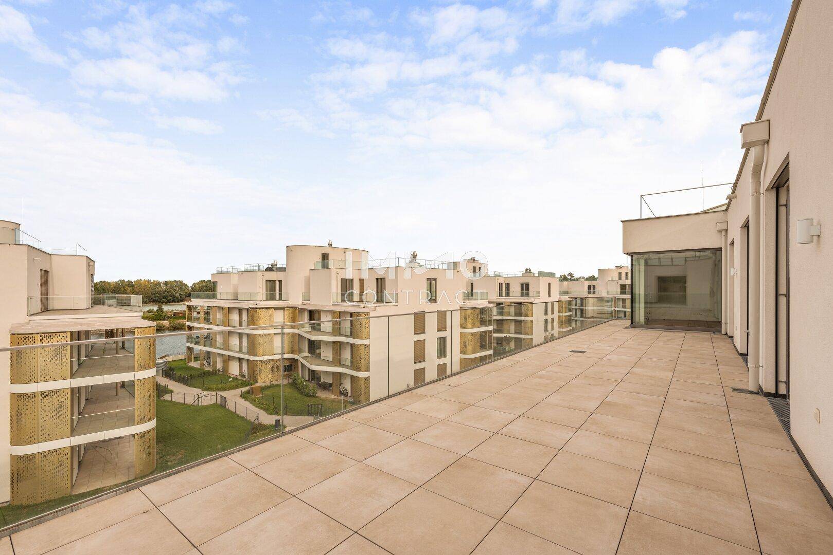Weitläufige Dachterrasse mit Fliesenboden und Blick auf moderne Wohngebäude und einen See.