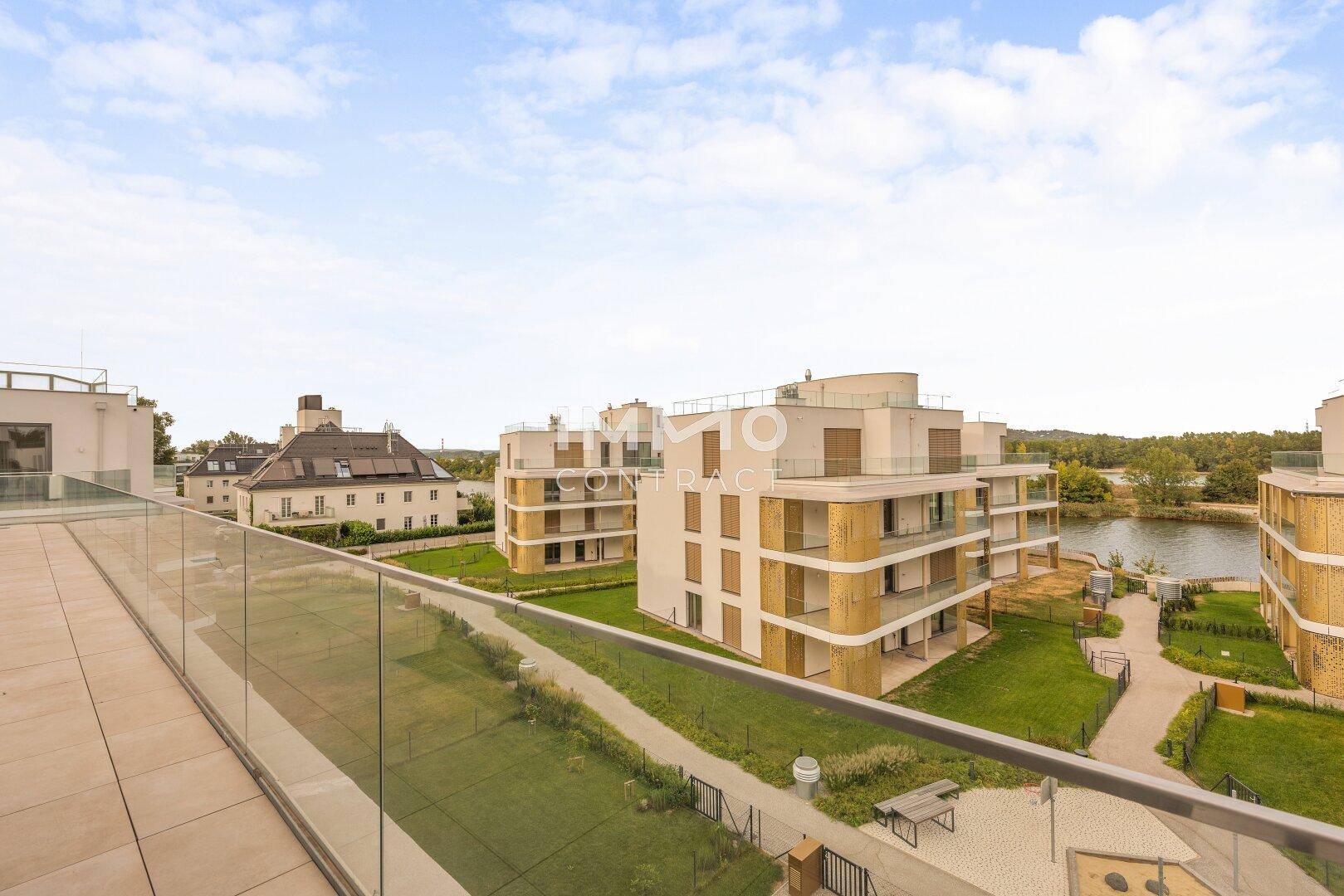 Weitläufige Dachterrasse mit Fliesenboden und Blick auf moderne Wohngebäude und einen See.