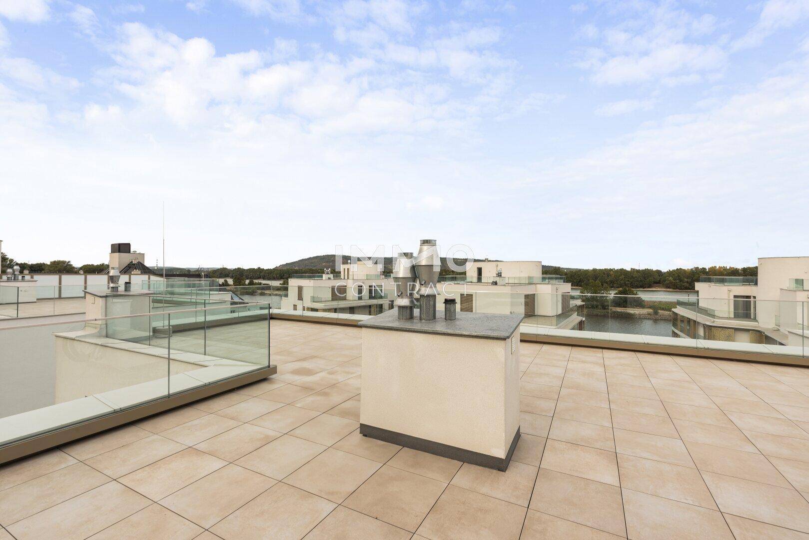 Weitläufige Dachterrasse mit Fliesenboden und Blick auf die umliegenden Gebäude und den See.