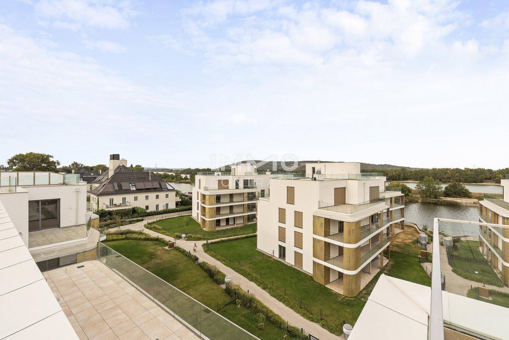 Weitläufige Dachterrasse mit Fliesenboden und Blick auf moderne Wohngebäude und einen See.
