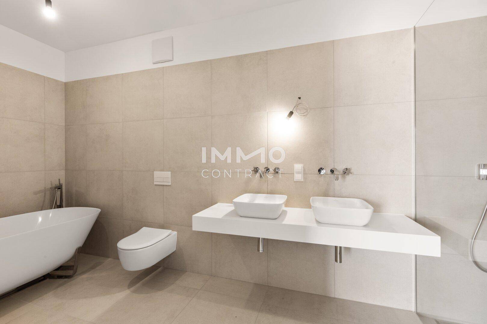 Geräumiges Badezimmer mit freistehender Badewanne, Doppelwaschbecken und beigefarbenen Wandfliesen.