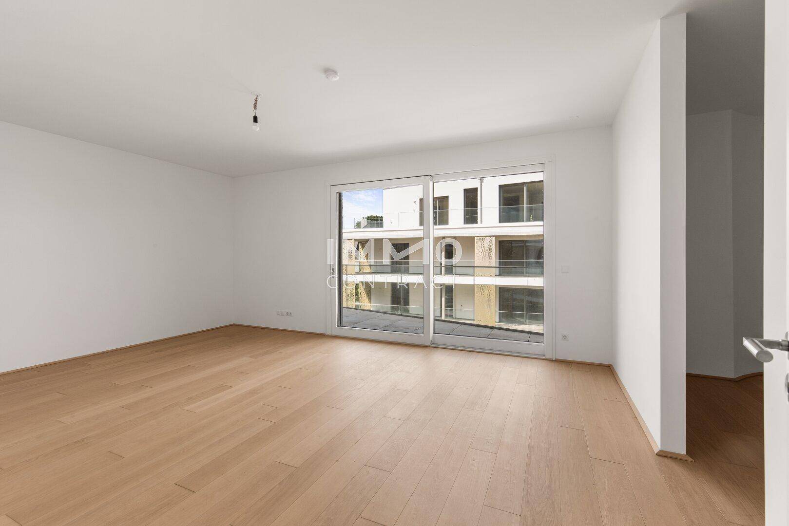 Geräumiges, helles Zimmer mit Holzboden und Schiebetür zum Balkon, ideal für Wohn- oder Schlafbereich.