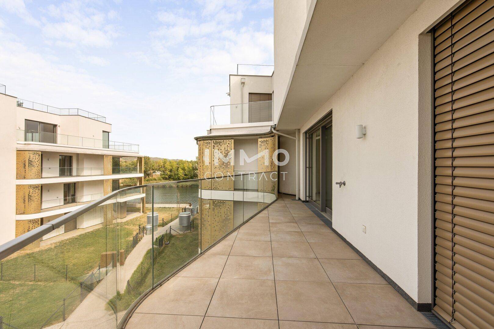 Geräumiger Balkon mit Fliesenboden und Glasgeländer, mit Blick auf das Wasser und die moderne Architektur.