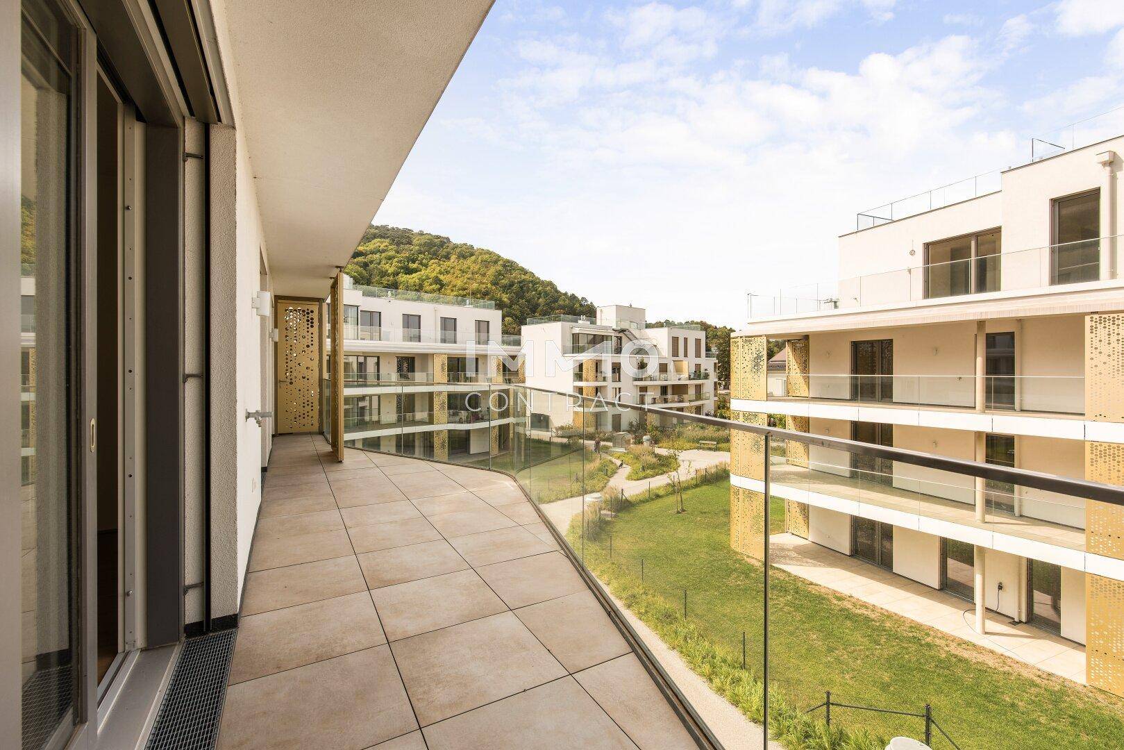 Langer Balkon mit Fliesenboden und Glasgeländer, bietet einen weiten Blick auf die Umgebung und die Hügel.