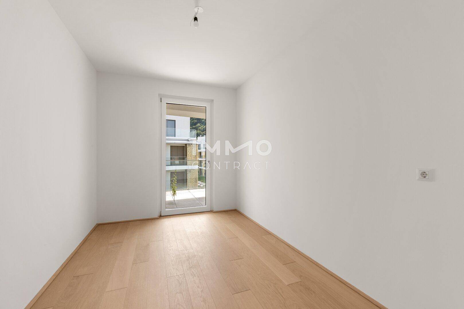 Helles Zimmer mit Holzboden und Zugang zu einem französischen Balkon, ideal als Schlaf- oder Arbeitszimmer.