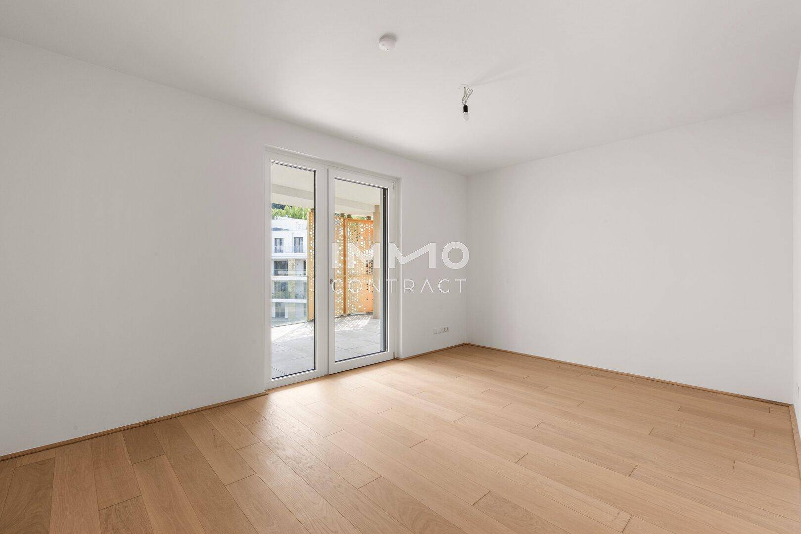 Geräumiges, helles Schlafzimmer mit Holzboden und großen Fenstertüren, die viel Licht spenden.