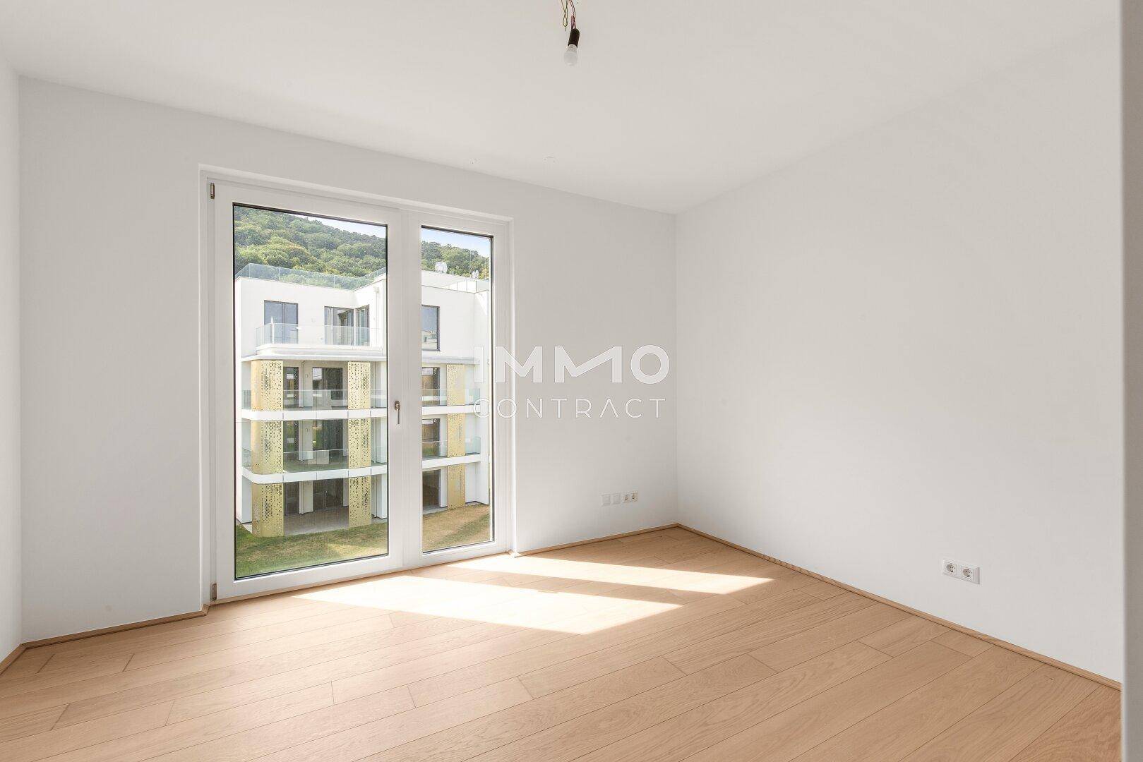 Helles Schlafzimmer mit Holzboden und großen Fenstertüren, die einen Blick auf die Umgebung bieten.