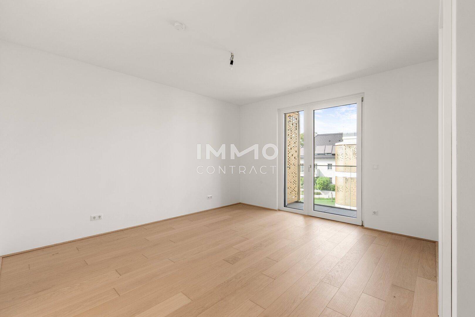 Geräumiges, helles Schlafzimmer mit Holzboden und Fenstertüren, die Zugang zu einem Balkon ermöglichen.
