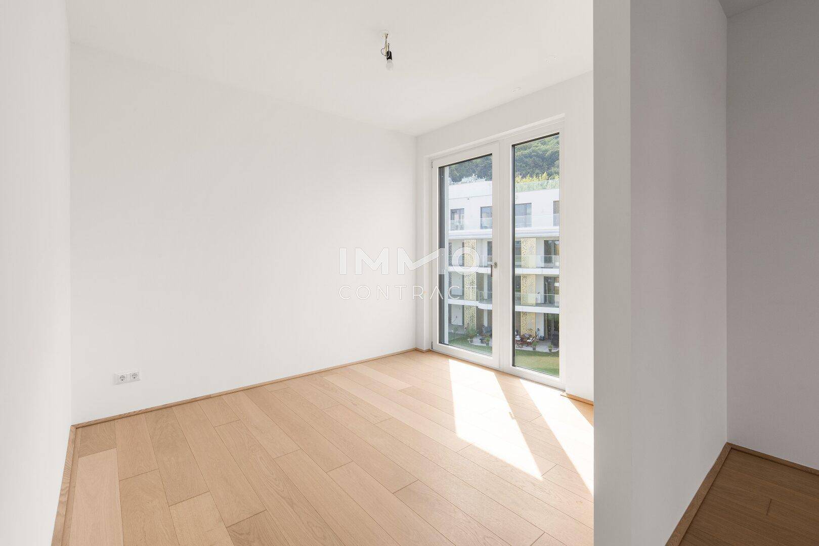Helles Schlafzimmer mit Holzboden und großen Fenstertüren, die einen Blick auf die moderne Architektur bieten.