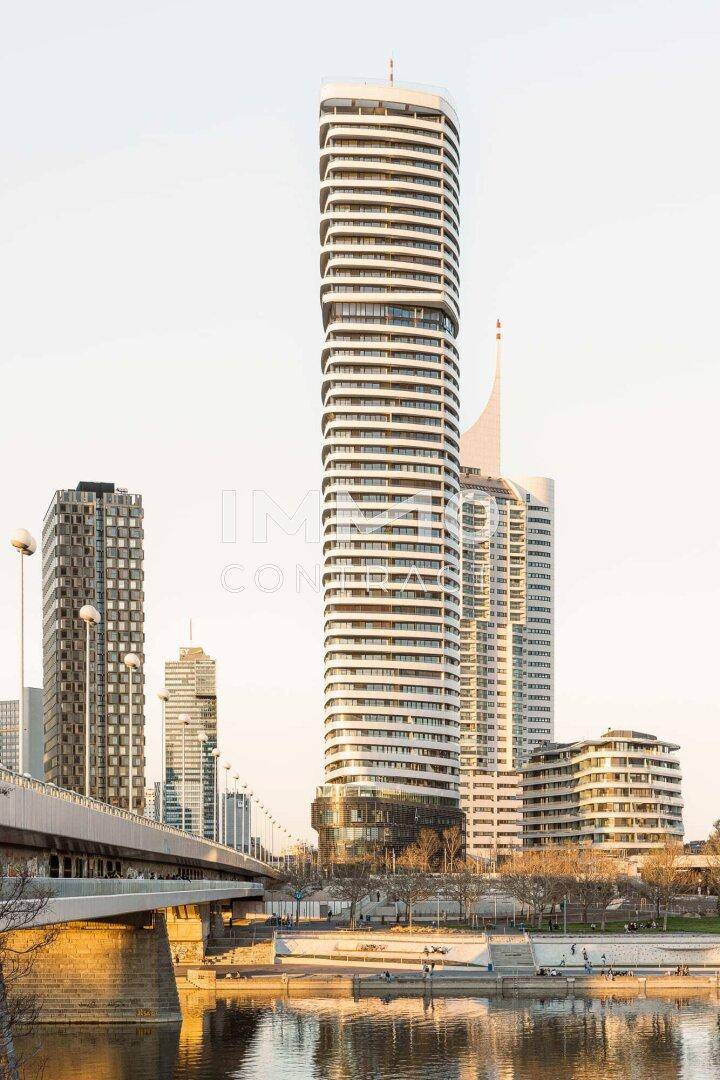 Elegantes Hochhaus mit moderner Architektur und geschwungenen Balkonen am Flussufer.