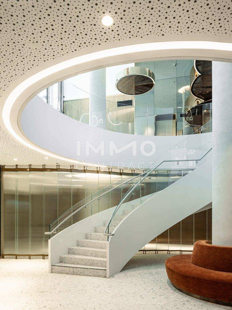 Elegante Wendeltreppe mit Glasgeländer in einer modernen Lobby mit hohen Decken.