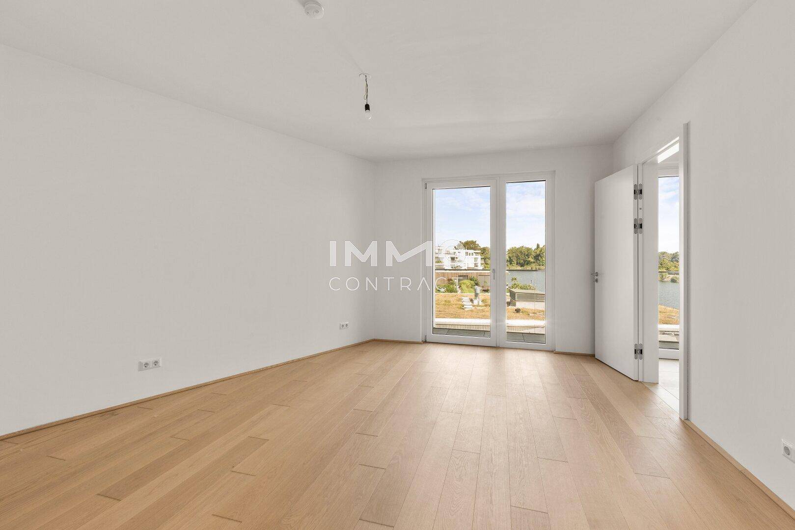 Helles Schlafzimmer mit Holzboden und Zugang zu einem Balkon mit Blick auf die Umgebung.