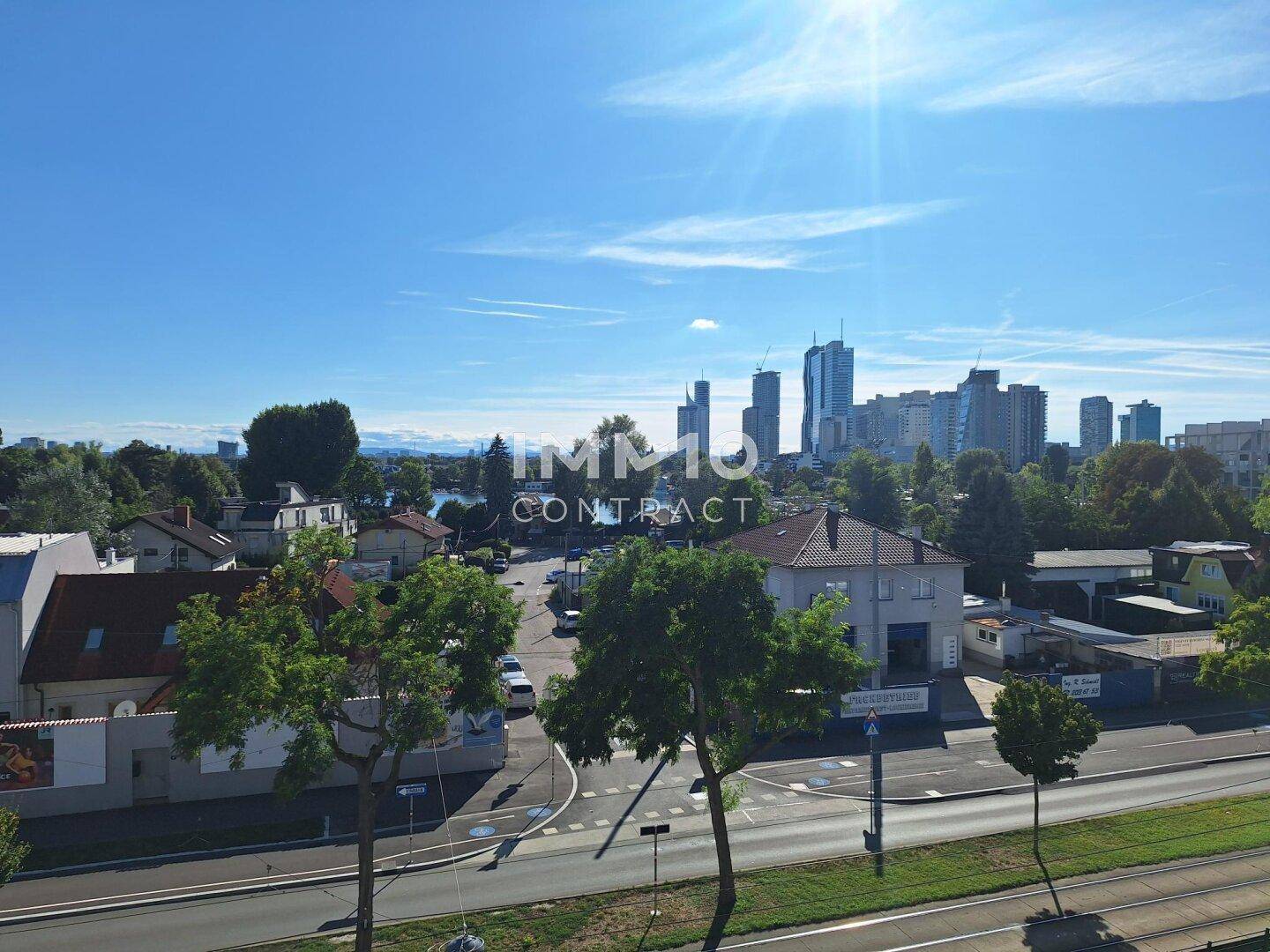 Weitläufiger Blick über die Stadt mit Hochhäusern und einem See im Hintergrund unter blauem Himmel.