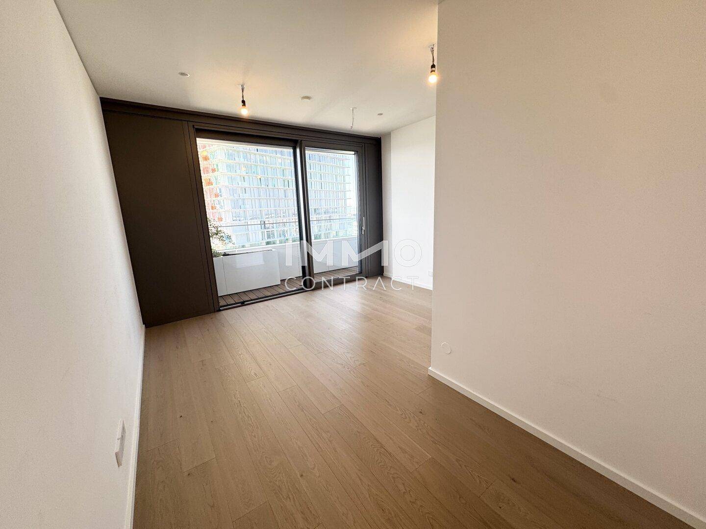 Heller Wohnbereich mit Zugang zum Balkon durch große Schiebetüren und Holzparkett.