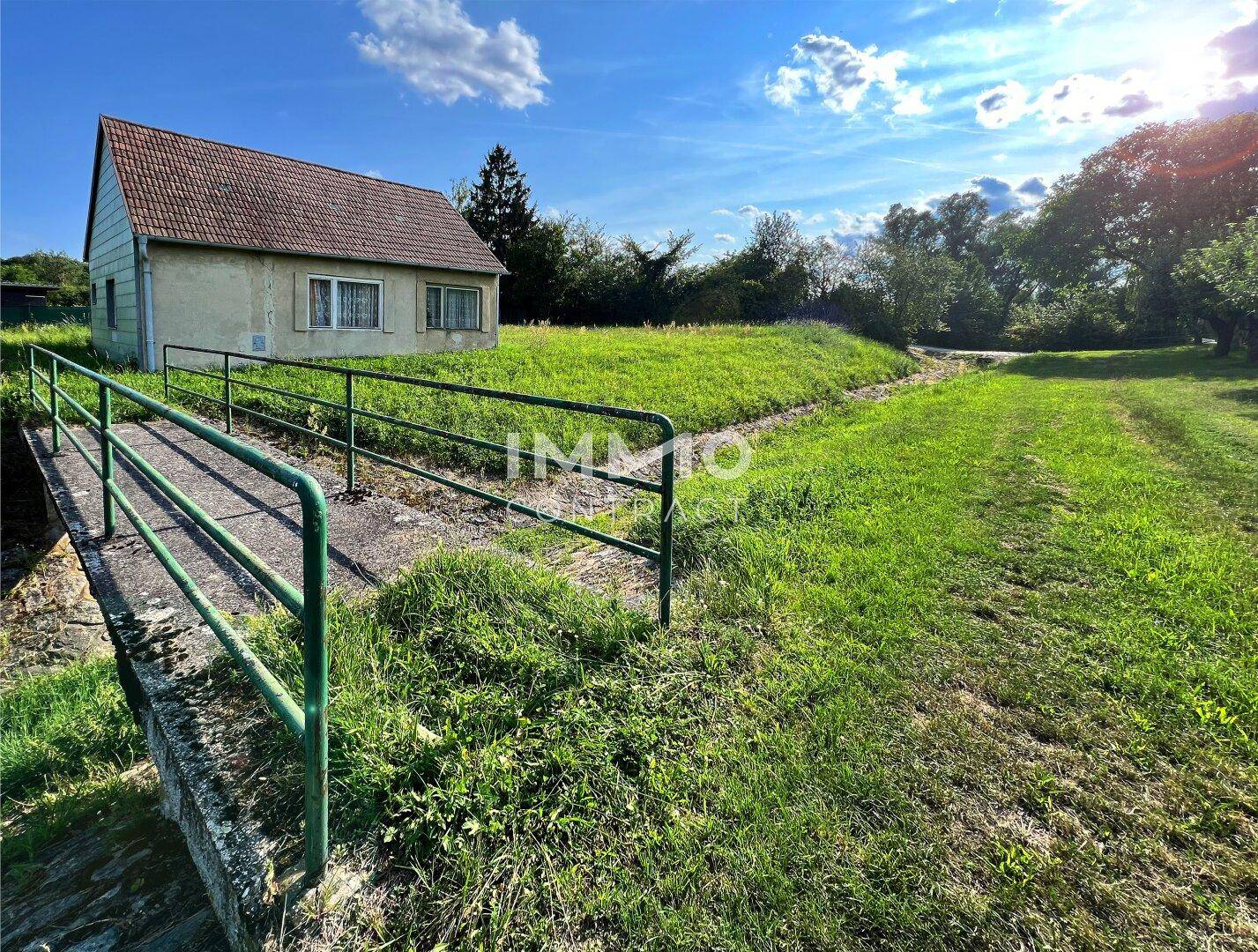 Hausansicht von einer kleinen Brücke über einen Graben, umgeben von grünen Wiesen.