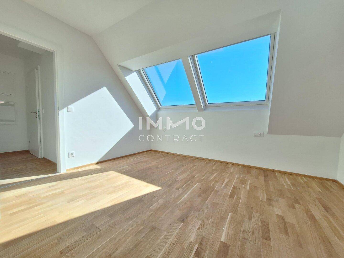 Dachgeschosszimmer mit schrägen Wänden, Holzboden und großen Dachfenstern für viel natürliches Licht.