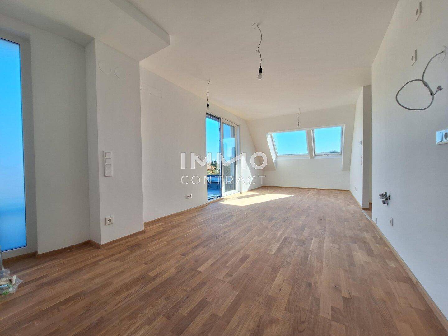Geräumiger, heller Wohnbereich mit Holzboden, großen Fenstern und Zugang zu einem Außenbereich.