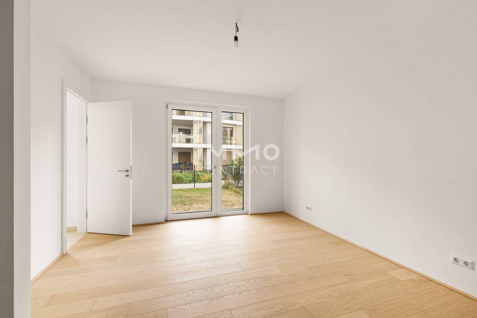 Freundliches Schlafzimmer mit Holzboden und großen Fenstertüren, die viel Tageslicht hereinlassen.