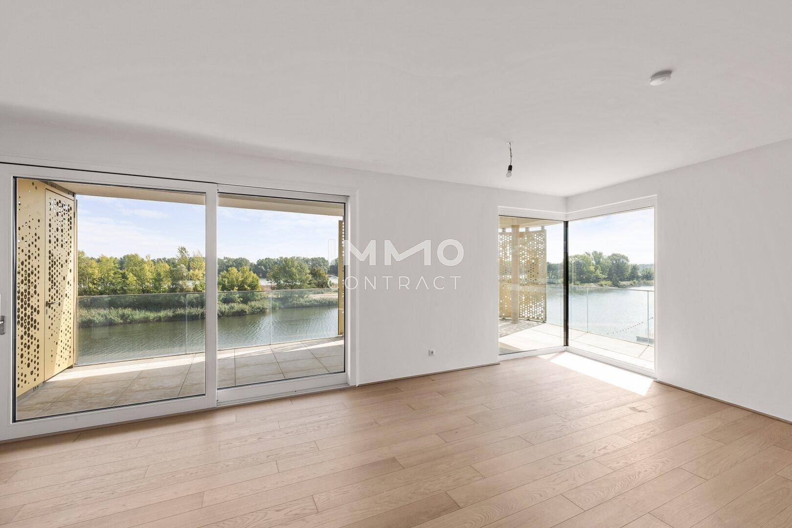 Helles, leeres Wohnzimmer mit großen Fenstern, Holzboden und direktem Zugang zum Balkon mit Flussblick.