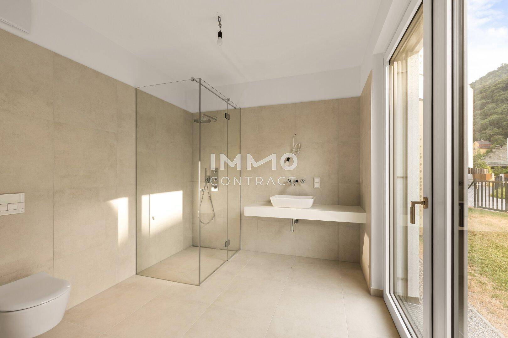 Modernes Badezimmer mit begehbarer Dusche, Wand-WC und großem Fenster mit Zugang nach draußen.