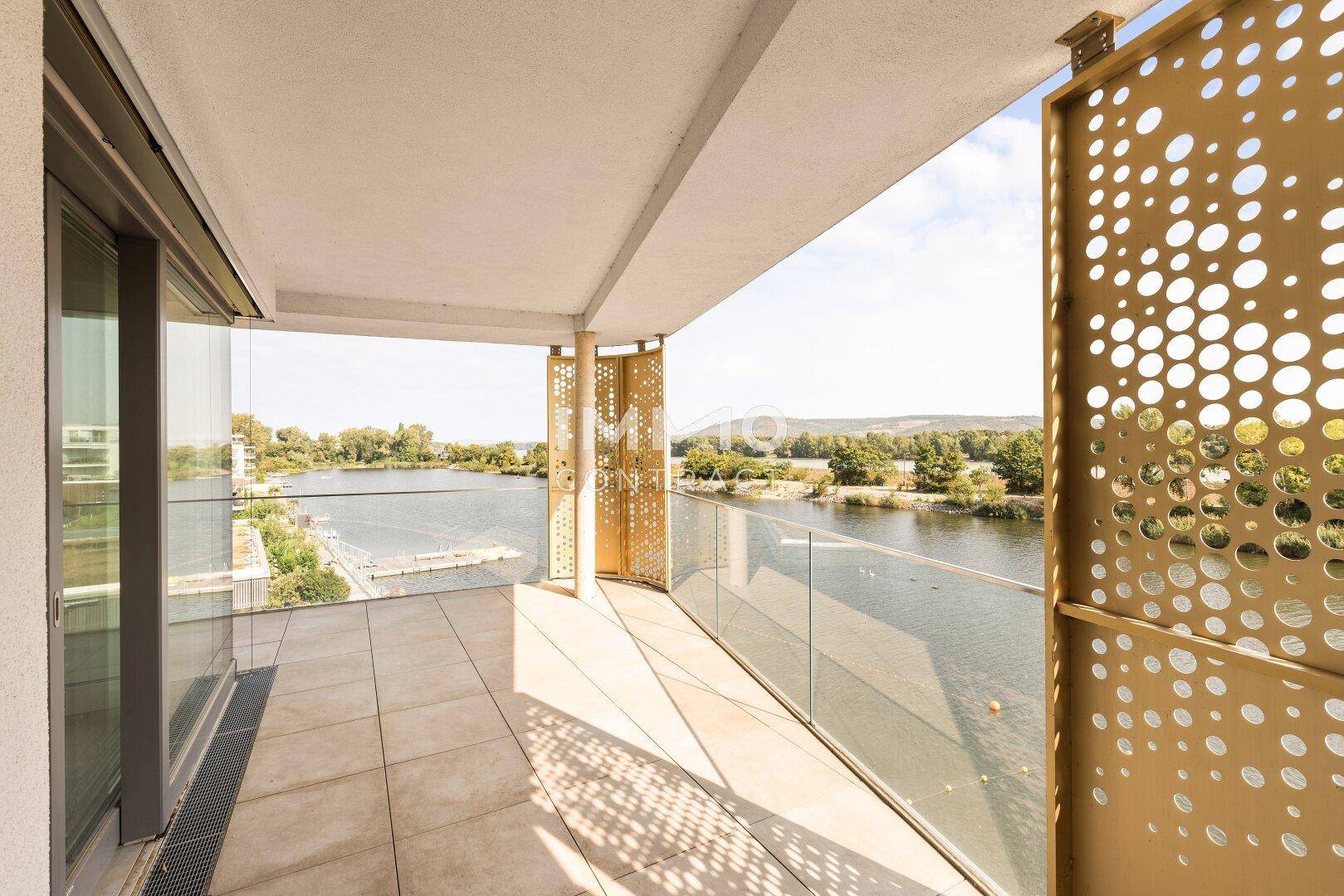Geräumiger Balkon mit modernem Design, Fliesenboden und Panoramablick auf das Wasser und die Landschaft.