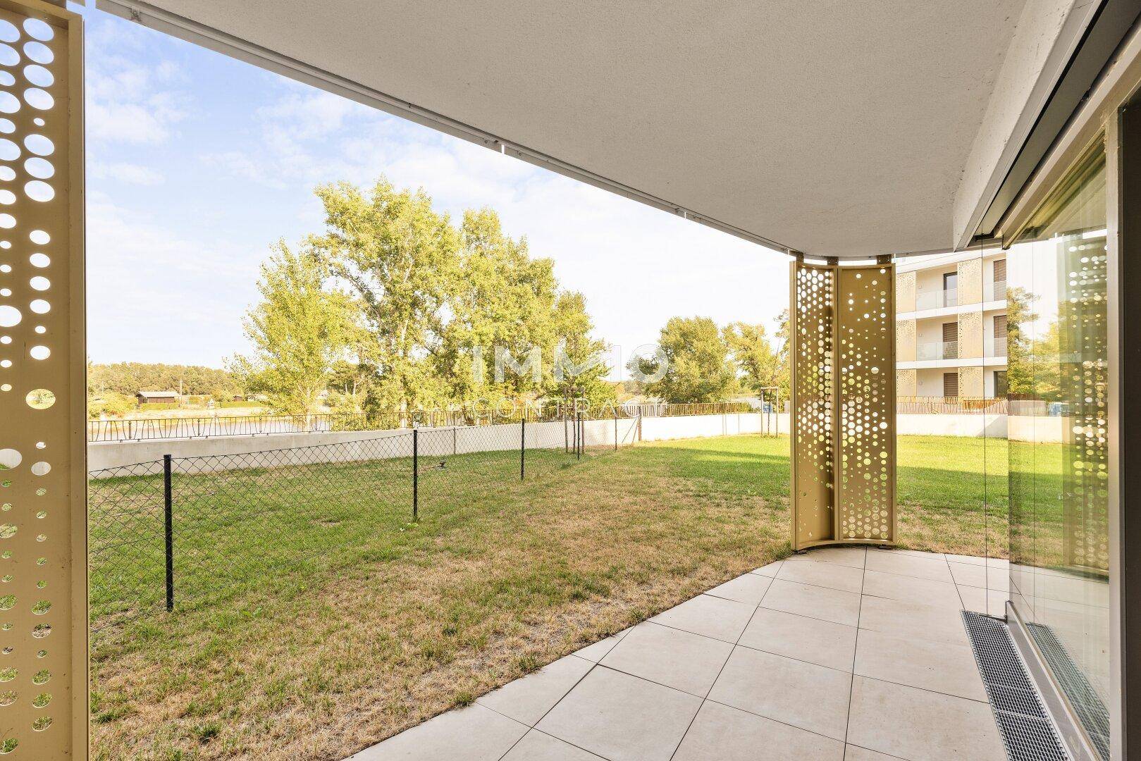 Überdachte Terrasse mit Fliesenboden und Blick auf den privaten Gartenbereich und die Umgebung.