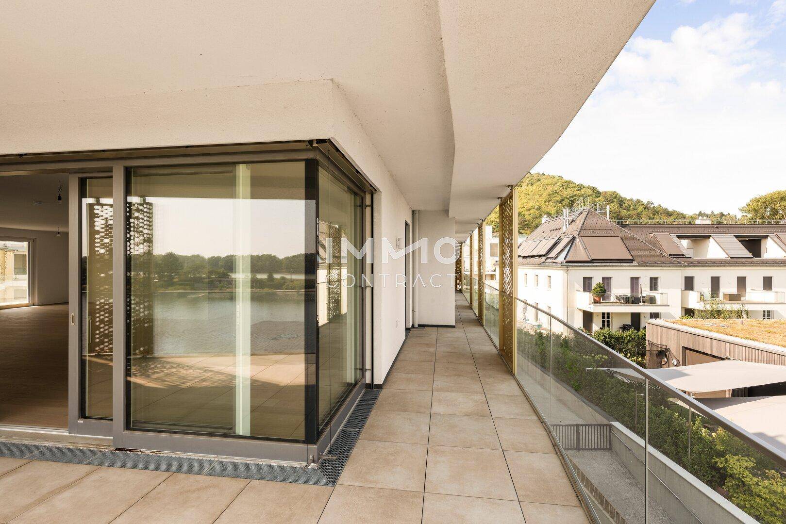 Lange Terrasse mit Fliesenboden, Glasgeländer und Blick auf die Nachbargebäude und den Fluss.