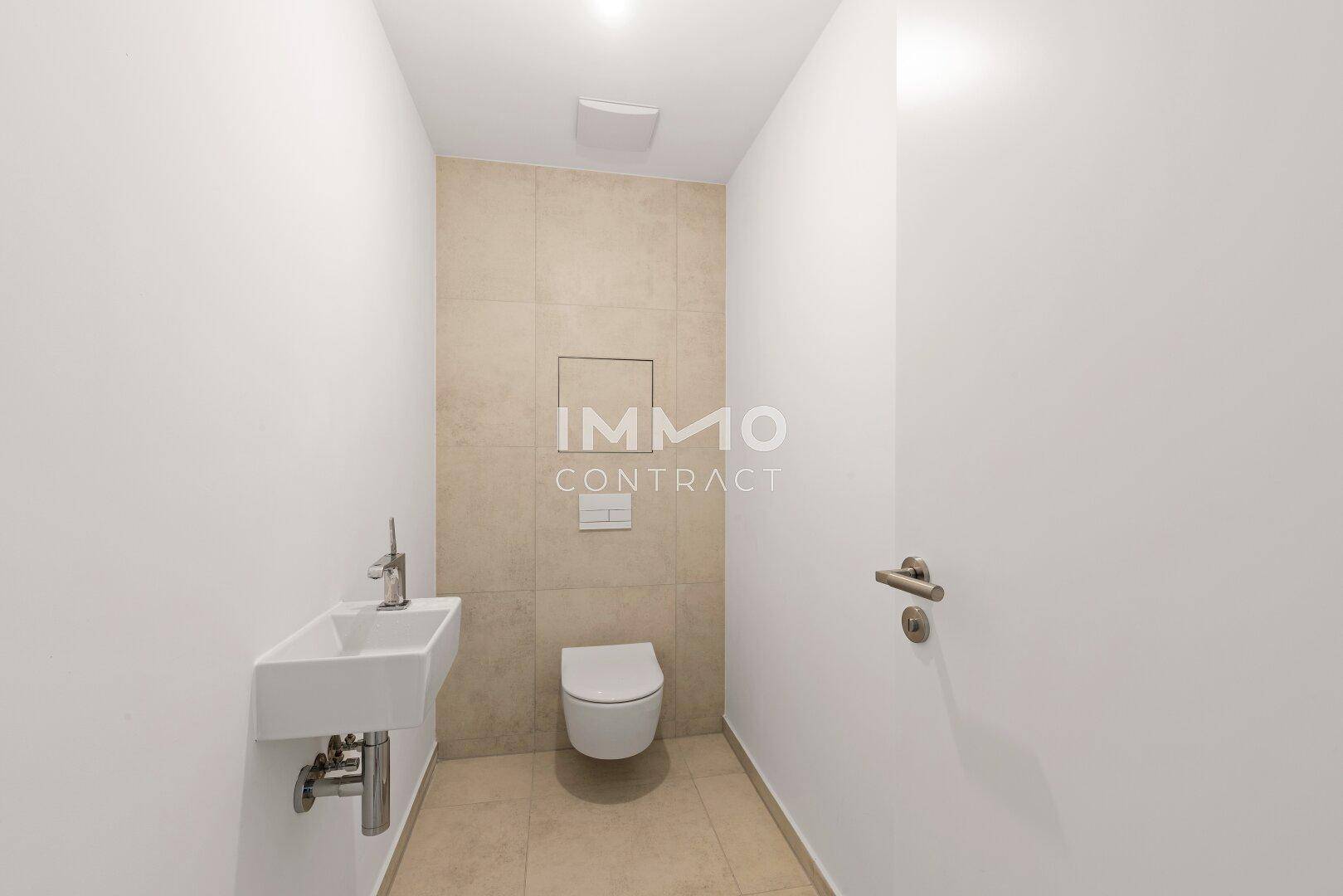 Modernes Gäste-WC mit wandhängender Toilette, kleinem Waschbecken und beigefarbenen Fliesen.