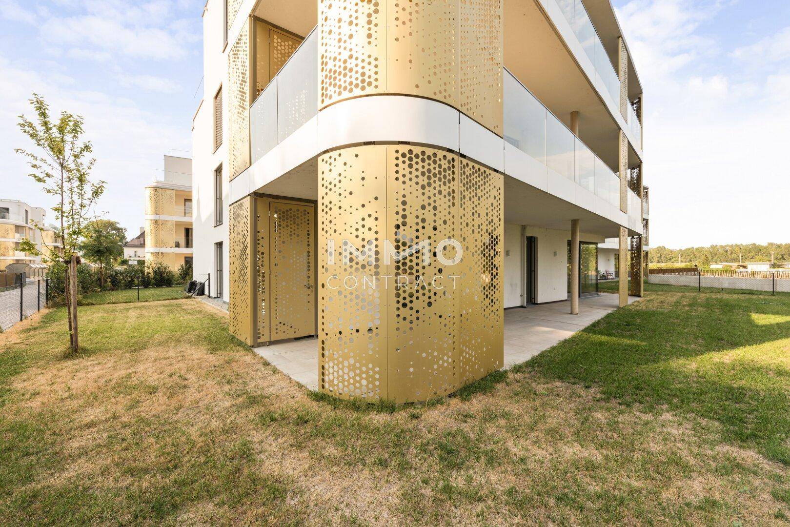 Moderne Gebäudefassade mit dekorativen goldenen Elementen und angrenzendem Gartenbereich.