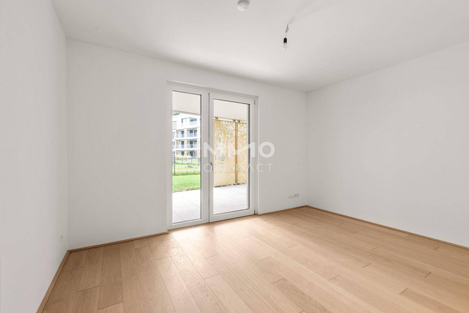 Helles Schlafzimmer mit Holzboden und Zugang zu einem Außenbereich mit Grünfläche.