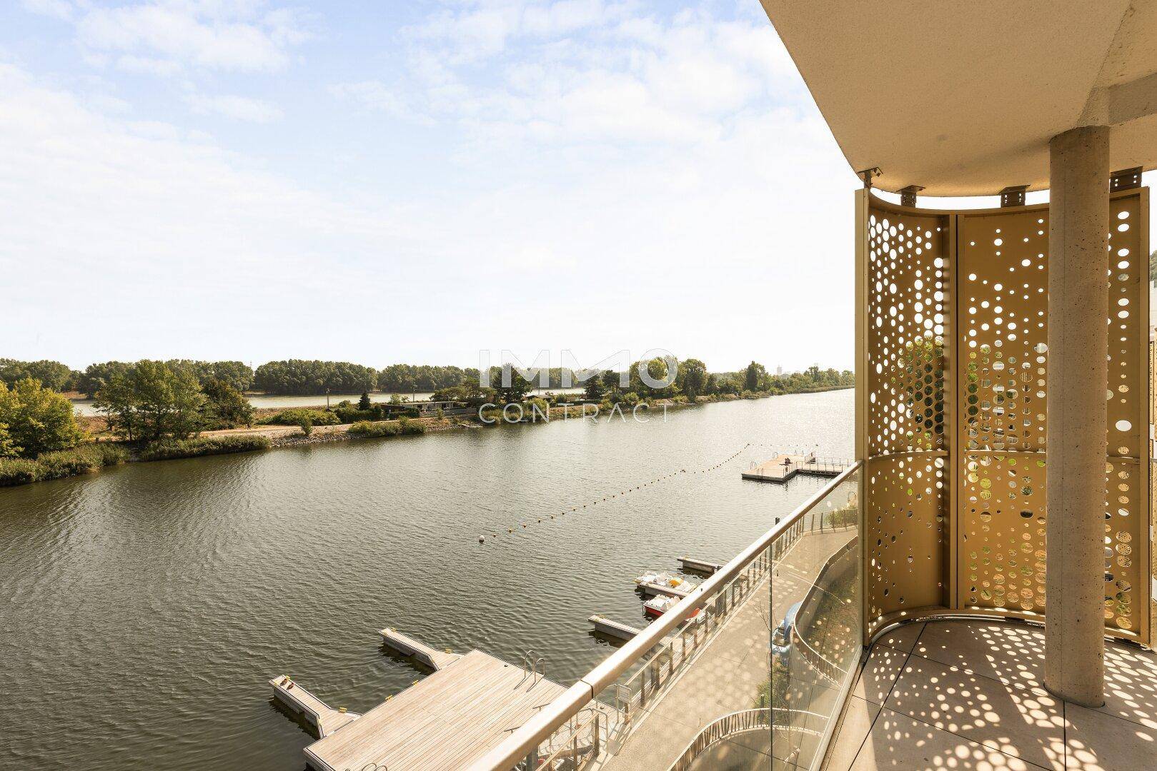 Moderner Balkon mit Glasgeländer und direktem Blick auf den Fluss mit Bootsanlegestellen.