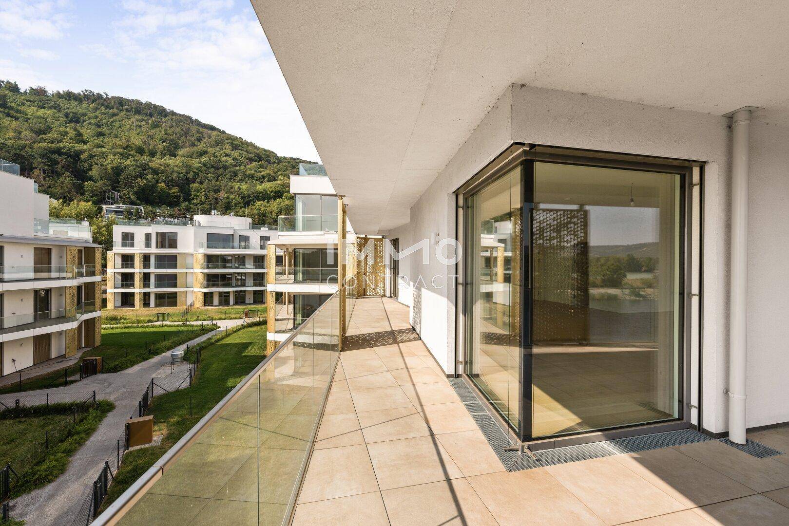 Weitläufige Terrasse mit Fliesenboden und Panoramablick auf die moderne Wohnanlage und die Natur.