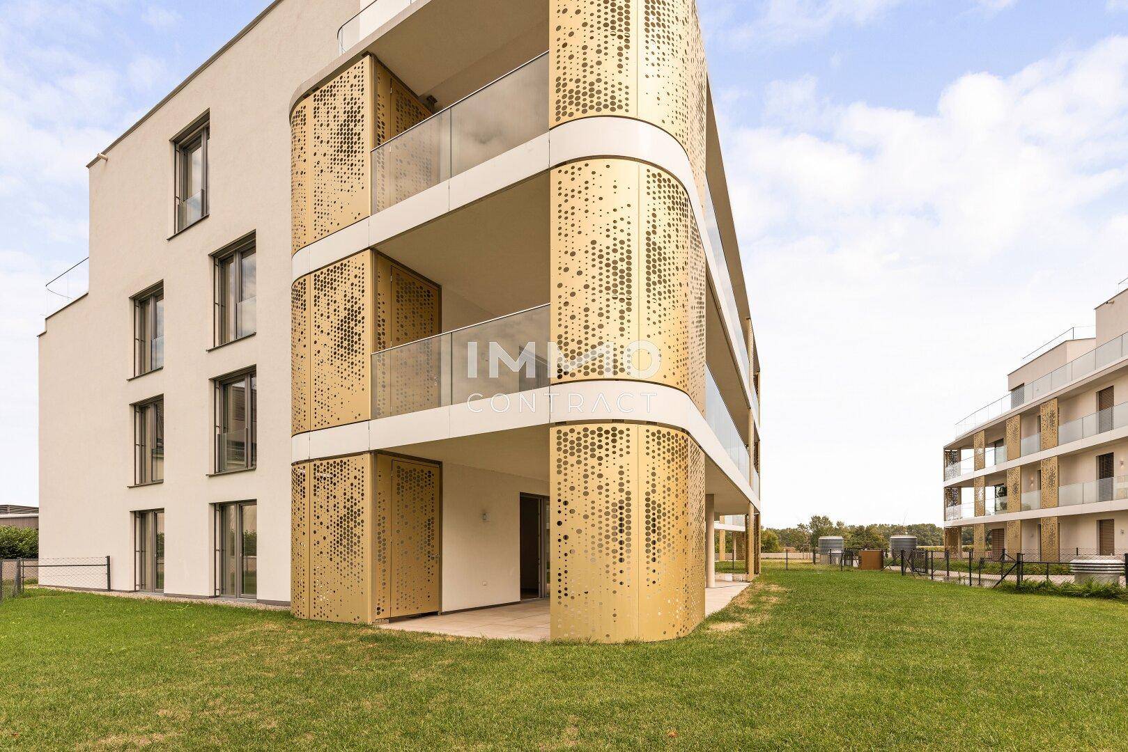 Moderne Wohnanlage mit auffälligen goldenen Balkonverkleidungen und gepflegter Grünfläche.