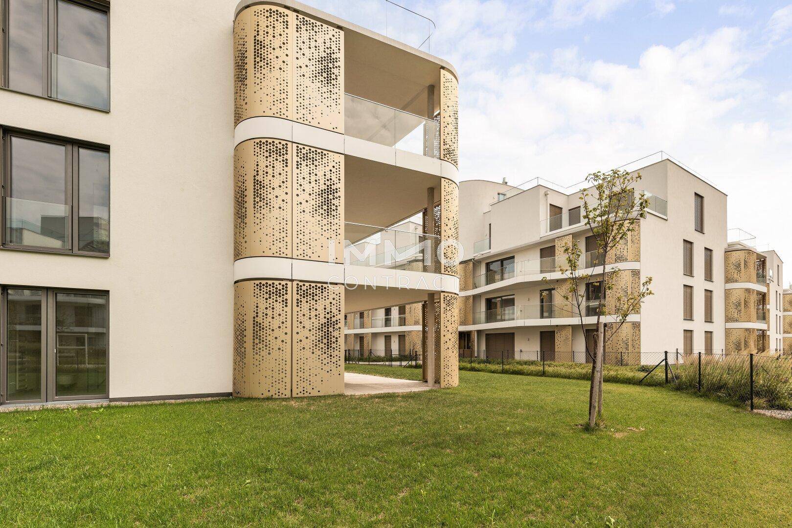 Ansicht einer modernen Wohnanlage mit markanten goldenen Balkonen und weitläufigen Grünflächen.