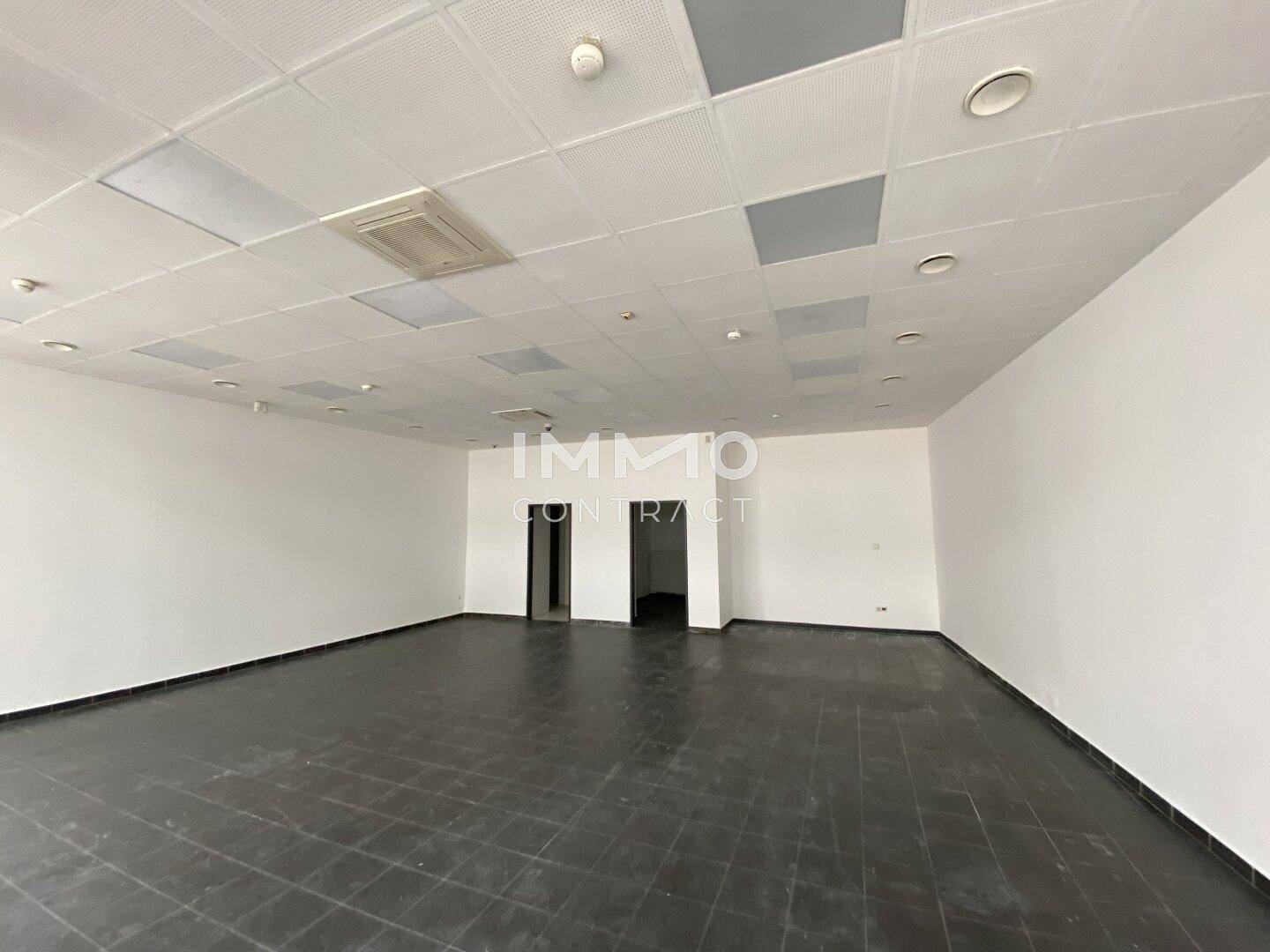 Leerer Geschäftsraum mit zwei Türöffnungen an der Rückwand, hellen Deckenplatten und dunklem Fliesenboden.