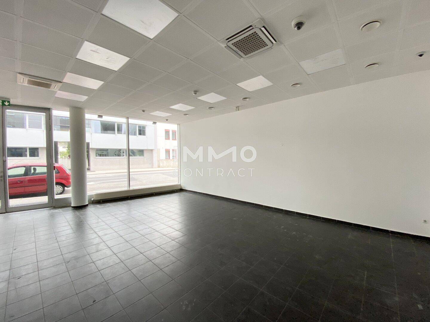 Weitläufiger, unmöblierter Geschäftsraum mit hellen Wänden und Blick auf die Straße durch große Fenster.