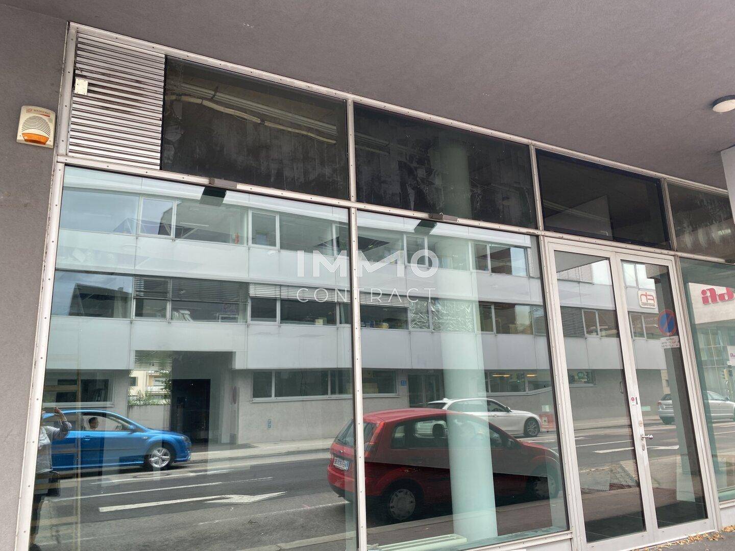 Ansicht der modernen Geschäftsfassade mit breiten Glasfenstern und Eingangstür, die den Straßenverkehr zeigt.