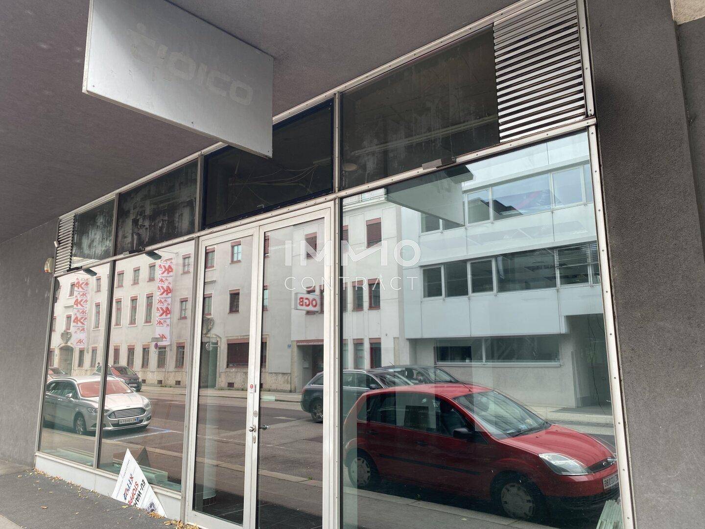 Außenansicht der Geschäftsfassade mit großen Glasflächen, die die umliegenden Gebäude widerspiegeln.