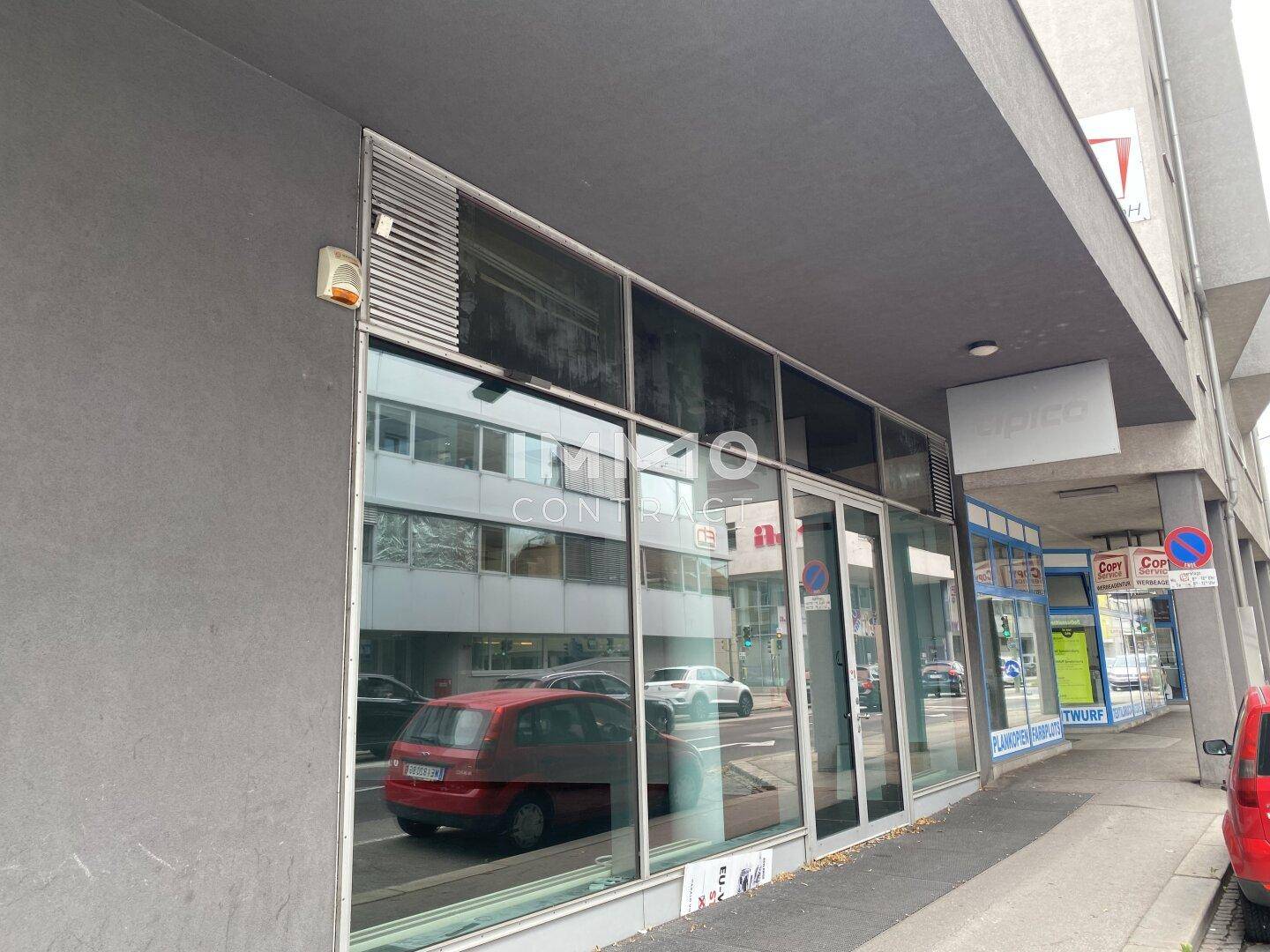 Moderne Geschäftsfassade mit großen Glasfenstern und Eingangsbereich, reflektiert die Umgebung.