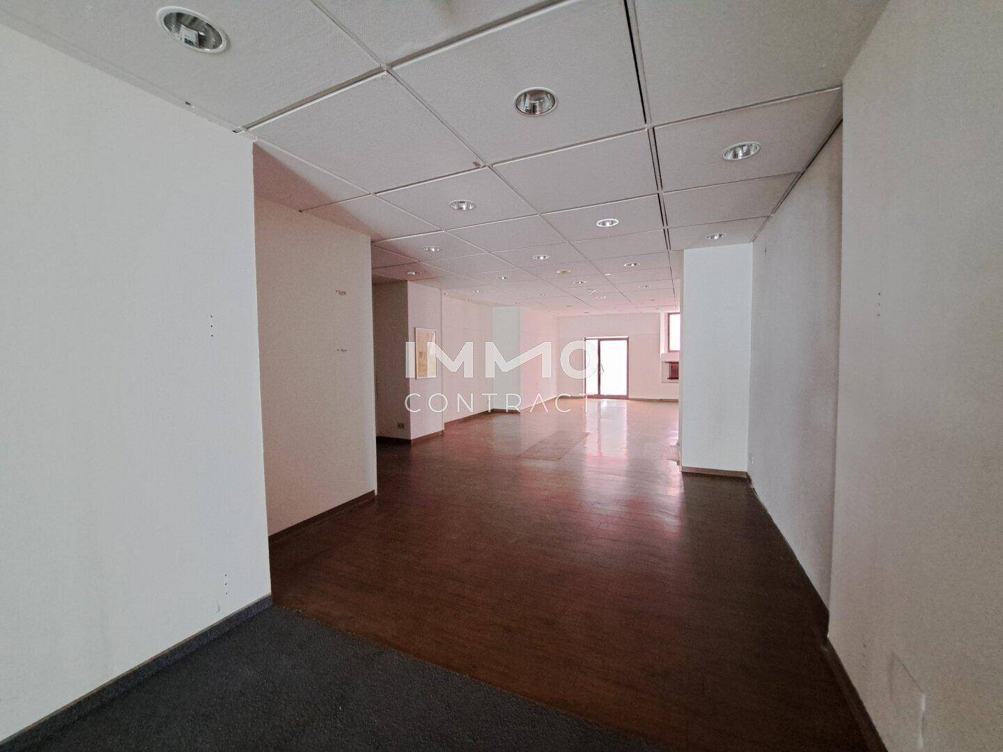 Langer, leerer Geschäftsraum mit dunklem Holzboden und abgehängter Decke.