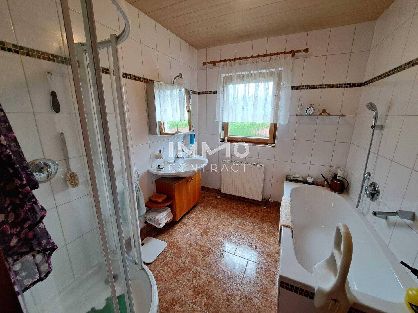 Helles Badezimmer mit Badewanne, Dusche, Fenster und Fliesenboden.