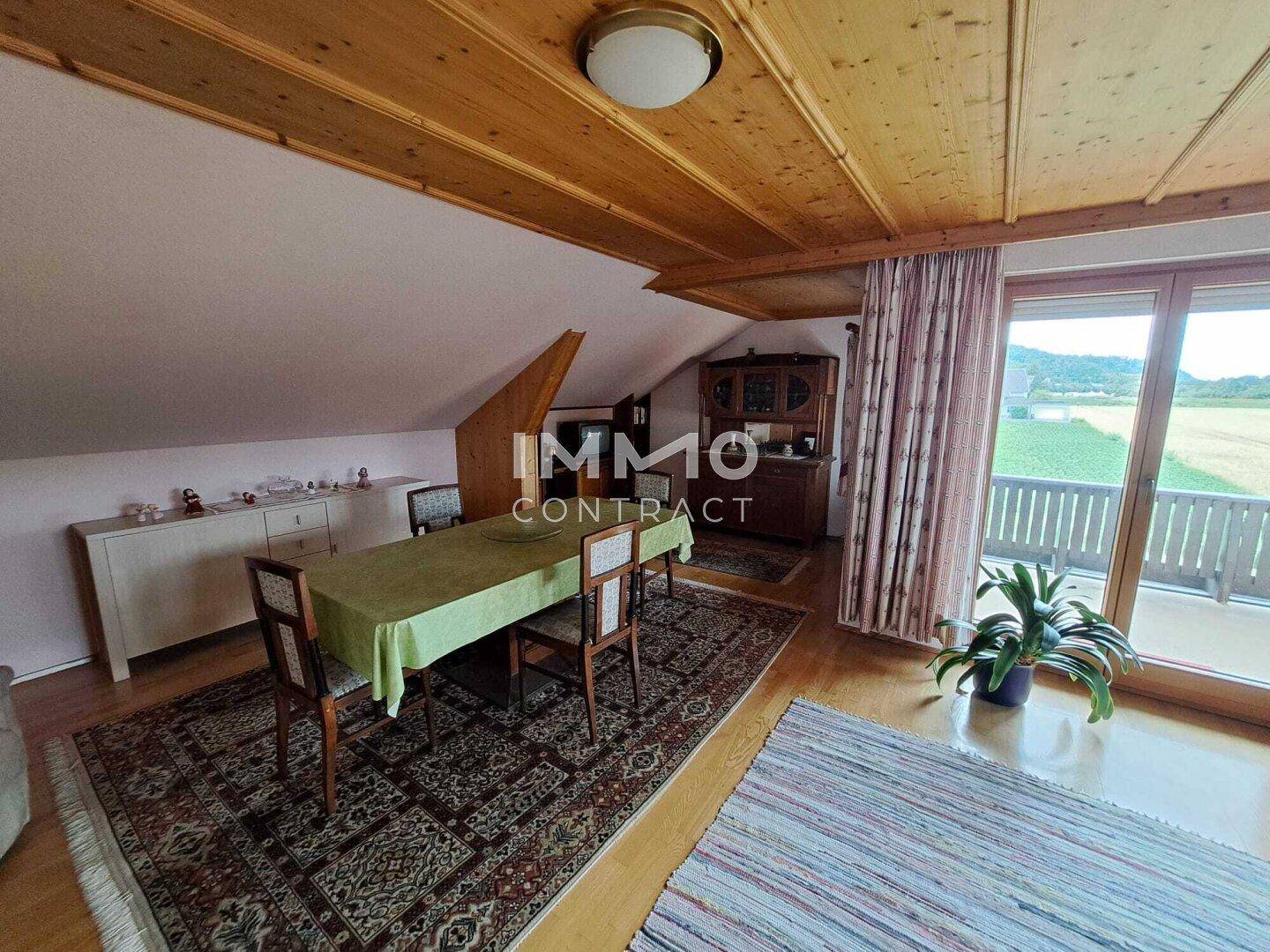 Essbereich im Dachgeschoss mit Holzbalkendecke, großem Esstisch und Balkonzugang.