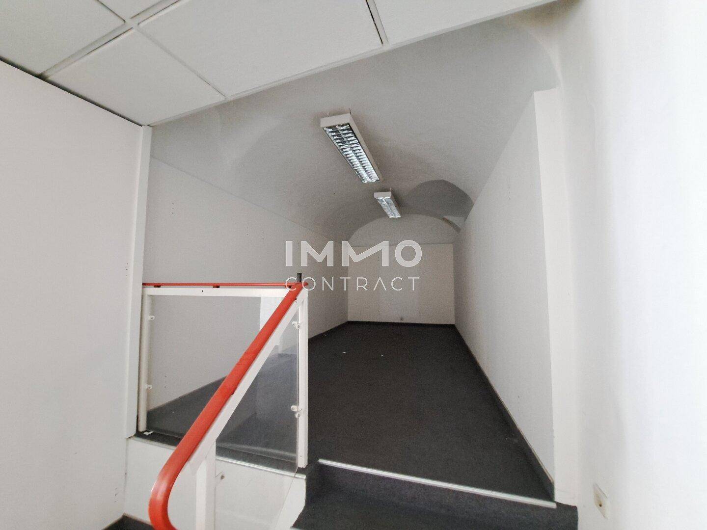 Treppenbereich mit rotem Handlauf, Teppichboden und gewölbter Decke in einem Durchgang.