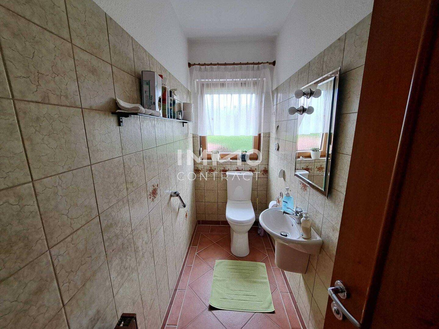 Kleines Gäste-WC mit Fliesenboden, Waschbecken und Fenster.