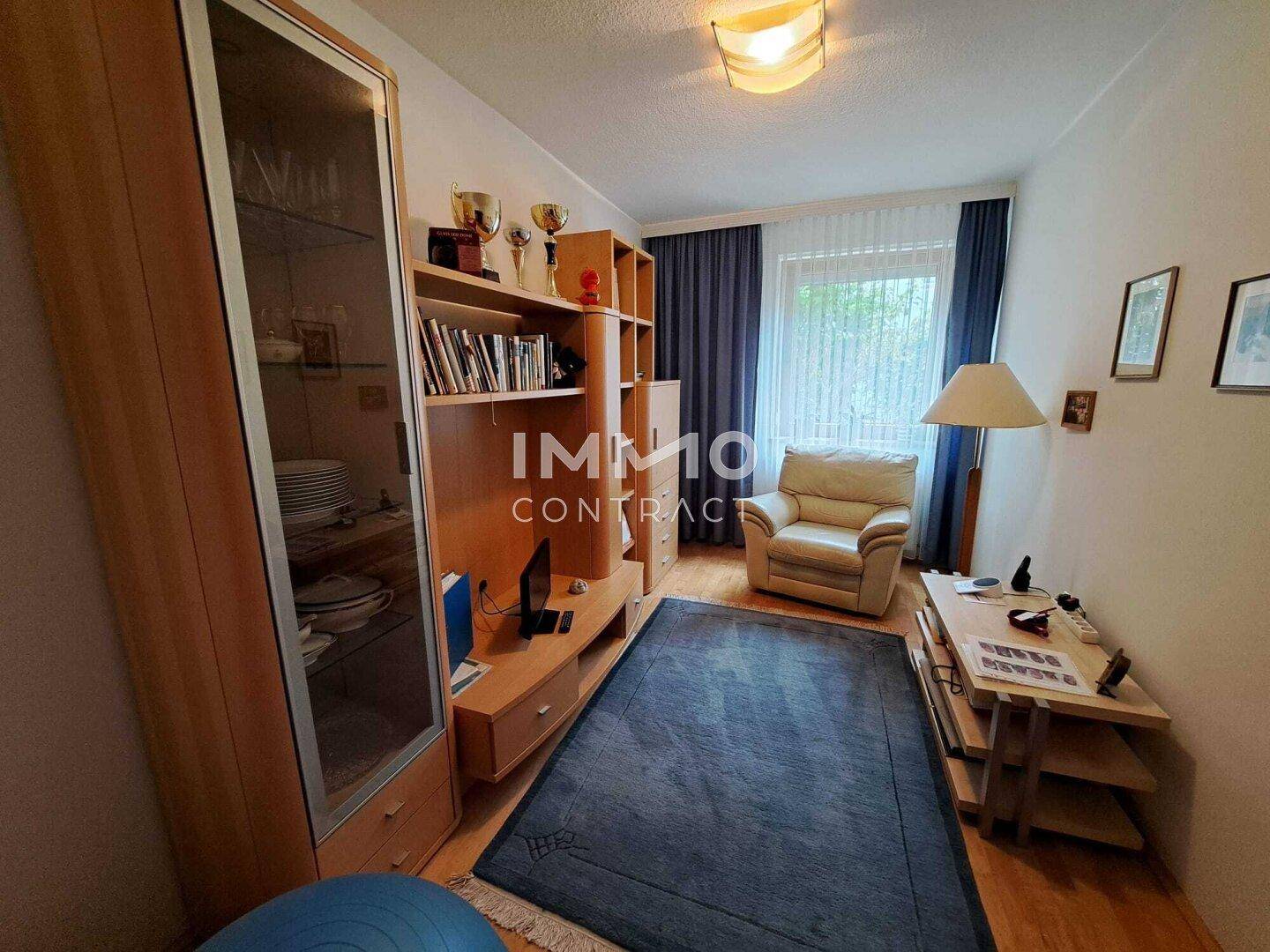 Wohnzimmer mit Holzregalen, Teppichboden und einem Sessel am Fenster.